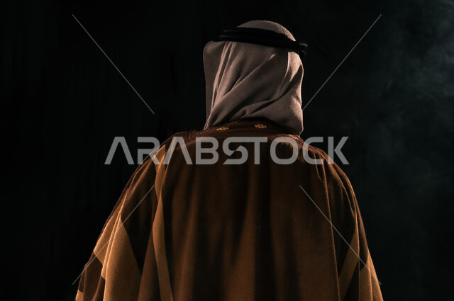 حب الوطن والانتماء إليه, ذكرى تأسيس الدولة السعودية الأولى 1727م، يوم بدينا 22 فبراير، الفخر بإنجازات المملكة، بورتريه مقرب من الخلف لرجل عربي خليجي سعودي يرتدي الغترة والبشت ينظر إلى شيء ما، خلفية سوداء