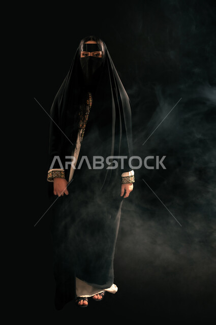 ذكرى تأسيس الدولة السعودية الأولى 1727م، يوم بدينا 22 فبراير، الفخر بإنجازات المملكة، بورتريه لامرأة عربية خليجية سعودية ترتدي البرقع والعباءة تنظر إلى الكاميرا بإيماءات الشموخ، حب الوطن والانتماء إليه, الجسم بالطول الكامل، خلفية سوداء