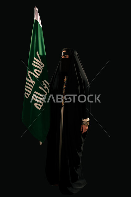 ذكرى تأسيس الدولة السعودية الأولى 1727م، بورتريه لامرأة عربية خليجية سعودية ترتدي البرقع والعباءة تحمل علم التأسيس تنظر إلى شيء ما بإيماءات الاعتزاز والشموخ، إظهار الولاء والحب للوطن, الفخر بإنجازات المملكة، يوم بدينا 22 فبراير، الجسم بالطول الكامل، خلفية سوداء