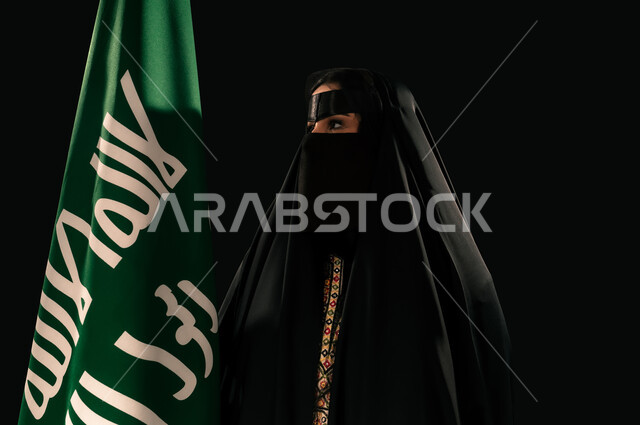 يوم بدينا 22 فبراير، ذكرى تأسيس الدولة السعودية الأولى 1727م، بورتريه مقرب لامرأة عربية خليجية سعودية ترتدي البرقع والعباءة تحمل علم التأسيس تنظر إلى شيء ما بإيماءات الاعتزاز والشموخ، إظهار الولاء والحب للوطن, الفخر بإنجازات المملكة، خلفية سوداء