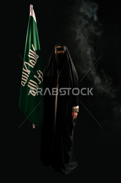 إظهار الولاء والحب للوطن, ذكرى تأسيس الدولة السعودية الأولى 1727م، بورتريه لامرأة عربية خليجية سعودية ترتدي البرقع والعباءة تحمل علم التأسيس تنظر إلى الكاميرا بإيماءات الاعتزاز والشموخ، الفخر بإنجازات المملكة، يوم بدينا 22 فبراير، الجسم بالطول الكامل، خلفية سوداء