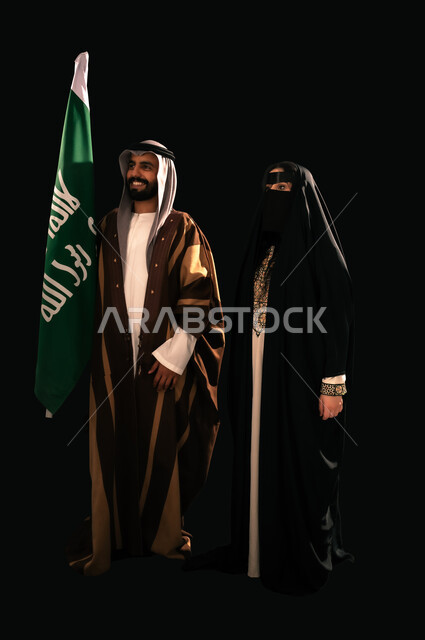 الثقة والفخر بإنجازات المملكة، بورتريه لرجل وامرأة عربيين خليجيين سعوديين يرتديان الزي الشعبي التقليدي يقفان بجانب علم التأسيس، ذكرى تأسيس الدولة السعودية الأولى 1727م، إظهار الولاء والحب للوطن, يوم بدينا 22 فبراير، الجسم بالطول الكامل، خلفية سوداء