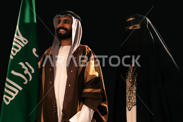 يوم بدينا 22 فبراير، الثقة والفخر بإنجازات المملكة، بورتريه مقرب لرجل وامرأة عربيين خليجيين سعوديين يرتديان الزي الشعبي التقليدي يقفان بجانب علم التأسيس، ذكرى تأسيس الدولة السعودية الأولى 1727م، إظهار الولاء والحب للوطن, خلفية سوداء