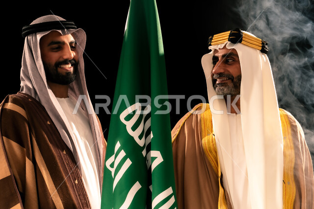 يوم بدينا 22 فبراير، إظهار الولاء والحب للوطن, الثقة والفخر بإنجازات المملكة، بورتريه مقرب لرجلين عربيين خليجيين سعوديين يرتدان الزي الشعبي التقليدي يقفان بجانب علم التأسيس، ذكرى تأسيس الدولة السعودية الأولى 1727م، خلفية سوداء