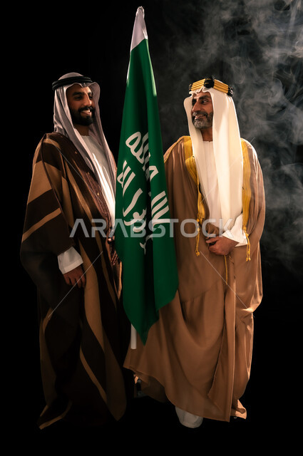 إظهار الولاء والحب للوطن, الثقة والفخر بإنجازات المملكة، ذكرى تأسيس الدولة السعودية الأولى 1727م، بورتريه لرجلين عربيين خليجيين سعوديين يرتدان الزي الشعبي التقليدي يقفان بجانب علم التأسيس، يوم بدينا 22 فبراير، الجسم بالطول الكامل، خلفية سوداء