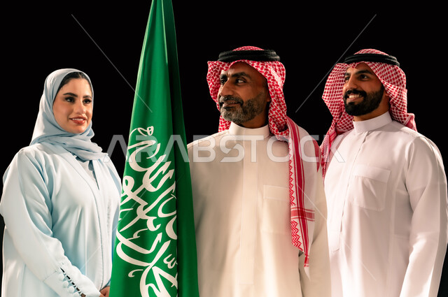 ترسيخ جذور الانتماء الوطني, إحياء ذكرى اليوم الوطني السعودي 23 سبتمبر, يوم العلم 11 مارس, اظهار الحب و التفاني للبلاد, النظر الى العلم بإيماءات السرور و الفخر, بورتريه مقرب لعائلة عربية خليجية سعودية مبتسمة تقف بجانب علم المملكة, خلفية سوداء