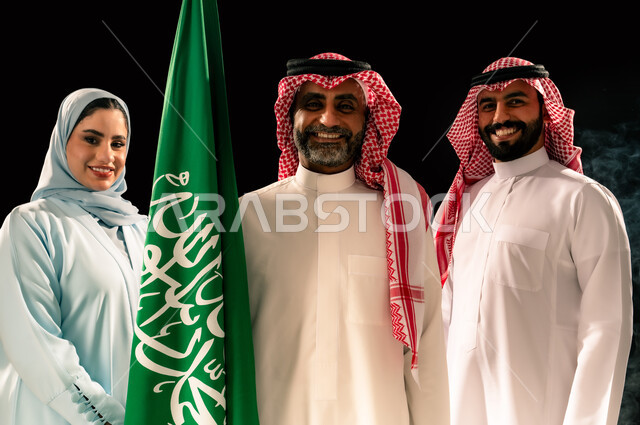 يوم العلم 11 مارس, ترسيخ جذور الانتماء الوطني, إحياء ذكرى اليوم الوطني السعودي 23 سبتمبر, اظهار الحب و التفاني للبلاد, النظر الى الكاميرا بإيماءات السرور و الفخر, بورتريه مقرب لعائلة عربية خليجية سعودية مبتسمة تقف بجانب علم المملكة, خلفية سوداء