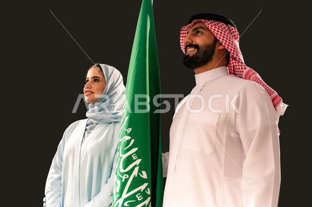 يوم العلم 11 مارس, ترسيخ جذور الانتماء الوطني, النظر الى شيء ما بإيماءات الفخر و السرور, إحياء ذكرى اليوم الوطني السعودي 23 سبتمبر, بورتريه مقرب لشاب و امرأة عربيان خليجيان سعوديان مبتسمان يقفان بجانب علم المملكة, خلفية سوداء