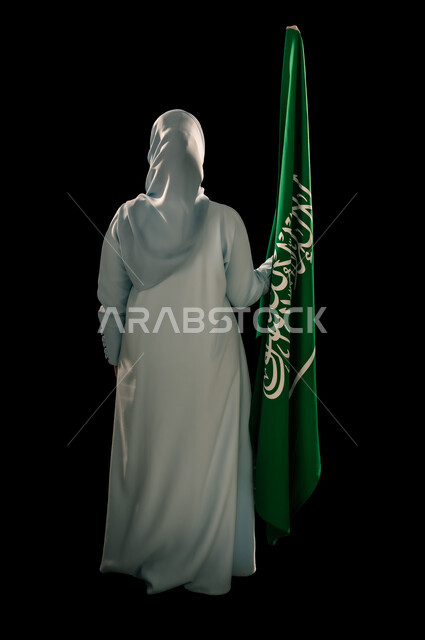 رفع راية التوحيد والإسلام، إحياء ذكرى اليوم الوطني السعودي 23 سبتمبر, يوم العلم 11 مارس، بورتريه من الخلف لامرأة عربية خليجية سعودية محجبة ترتدي العباءه تحمل بيدها علم المملكة، الفخر و الاعتزاز بالانتماء للوطن، الجسم بالطول الكامل, خلفية سوداء