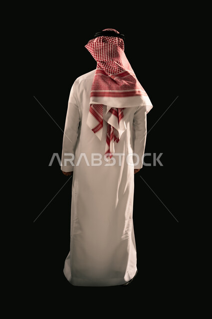 Concern for appearance, concept of masculinity and elegance, portrait from behind of a Saudi Arabian Gulf man wearing traditional thobe and shemagh standing straight, full body image, black background