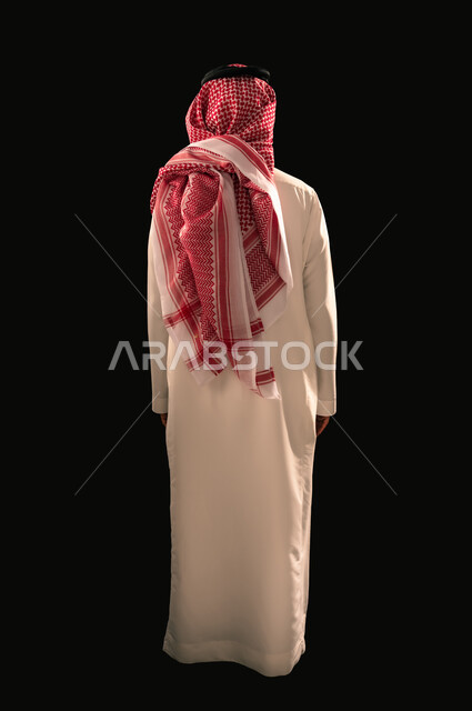 Concept of masculinity and elegance, concern for appearance, portrait from back of Saudi Arabian Gulf man wearing traditional thobe and shemagh standing straight, full body image, black background