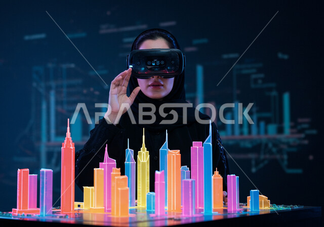 التفاعل والاندماج بالعالم الخيالي، رؤية مستقبلية سعودية 2030، استخدام التقنية والاجهزة الحديثة، امرأة عربية خليجية سعودية محجبة ترتدي عباءة سوداء تضع نظارة الواقع الافتراضي تجلس امام مكتب بطاولة تحوي شاشات هولوجرامية ومجسمات ثلاثية الأبعاد لابراج وناطحات السحاب