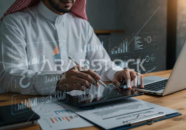رسوم بيانية إحصائية للبورصة المالية، عناصر هولوجرامية ثلاثية الأبعاد، دمج التكنولوجيا المتطورة بالعمل، مفهوم التحول الرقمي، رجل عربي خليجي سعودي يرتدي الثوب التقليدي والشماغ يقوم بكتابة الارقام والاحصائيات على جهاز التابلت، تطوير الشركة والمشاريع الاقتصادية