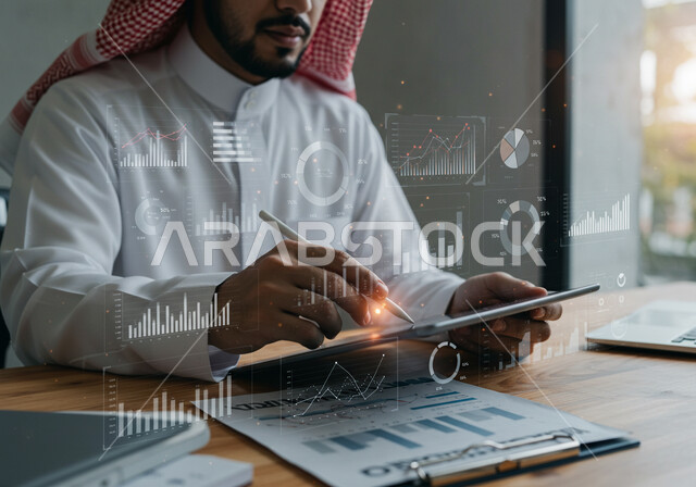 رموز هولوجرامية ثلاثية الأبعاد، دمج التكنولوجيا المتطورة بالعمل، مفهوم التحول الرقمي، رجل عربي خليجي سعودي يرتدي الثوب التقليدي والشماغ يقوم بكتابة الارقام والاحصائيات على جهاز التابلت، رسوم بيانية إحصائية للبورصة المالية، تطوير الشركة والمشاريع الاقتصادية
