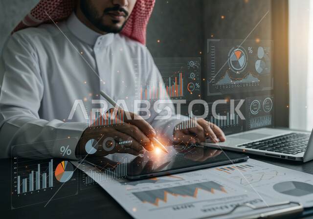 دمج التكنولوجيا المتطورة بالعمل، مفهوم التحول الرقمي، رجل عربي خليجي سعودي يرتدي الثوب التقليدي والشماغ يقوم بكتابة الارقام والاحصائيات على جهاز التابلت، رموز هولوجرامية ثلاثية الأبعاد، رسوم بيانية إحصائية للبورصة المالية، تطوير الشركة والمشاريع الاقتصادية