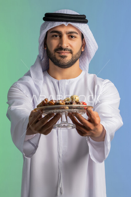 Delicious Ramadan hospitality, local national product and crop, high nutritional value meal, close-up portrait of an Emirati Gulf Arab man wearing a kandura and ghutra holding a plate of healthy dates and looking at the camera, breaking the fast in Ramadan, celebrating the arrival of the month of goodness