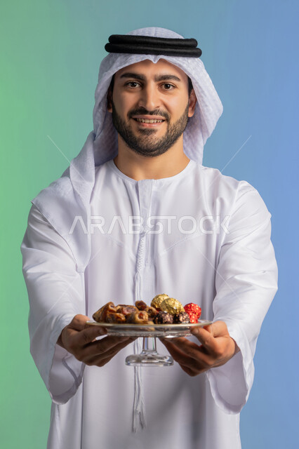 ضيافة رمضانية لذيذة، منتج ومحصول محلي وطني، وجبة ذات قيمة غذائية عالية، بورتريه مقرب لرجل عربية خليجية اماراتي يرتدي الكندورة والغترة يحمل بيده طبق من التمر الصحي وينظر الى الكاميرا، افطار الصائم في رمضان، الاحتفال بقدوم شهر الخير