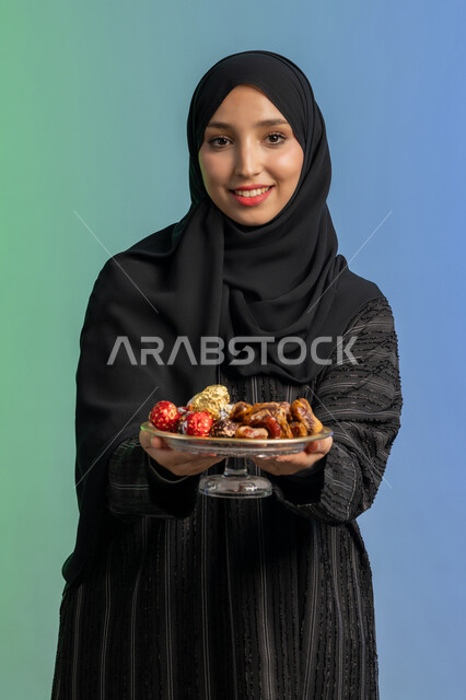 منتج ومحصول محلي وطني، ضيافة رمضانية لذيذة، وجبة ذات قيمة غذائية عالية، بورتريه لامراة عربية خليجية اماراتية ترتدي العباءة السوداء تحمل بيدها طبق من التمر الصحي وتنظر الى الكاميرا، افطار الصائم في رمضان، الاحتفال بقدوم شهر الخير