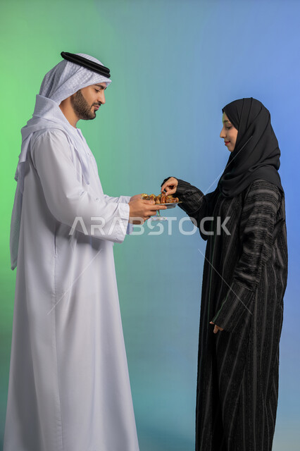 وجبة ذات قيمة غذائية عالية، منتج زراعي محلي وطني ضيافة رمضانية لذيذة، بورتريه من الجانب لرجل عربي خليجي اماراتي يرتدي الكندورة والغترة يقوم بتقديم التمر الصحي لزوجته، افطار الصائم في رمضان، مفهوم احترام الزوجة وتقديرها، الاحتفال بقدوم شهر الخير