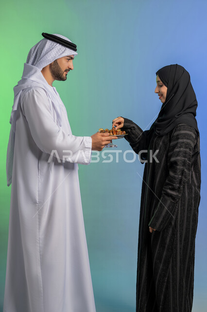 منتج زراعي محلي وطني ضيافة رمضانية لذيذة، وجبة ذات قيمة غذائية عالية، بورتريه من الجانب لرجل عربي خليجي اماراتي يرتدي الكندورة والغترة يقوم بتقديم التمر الصحي لزوجته، افطار الصائم في رمضان، مفهوم احترام الزوجة وتقديرها، الاحتفال بقدوم شهر الخير