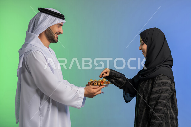 منتج زراعي محلي وطني ضيافة رمضانية لذيذة، وجبة ذات قيمة غذائية عالية، بورتريه من الجانب لرجل عربي خليجي اماراتي يرتدي الكندورة والغترة يقوم بتقديم التمر الصحي لزوجته، افطار الصائم في رمضان، مفهوم احترام الزوجة وتقديرها، الاحتفال بقدوم شهر الخير