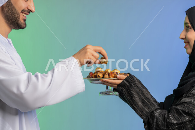 Hospitality in the holy month of Ramadan, a meal with high nutritional value, a portrait of an Arab Gulf Emirati woman wearing an abaya and hijab holding a plate of fresh healthy sugary dates with gestures of presenting them to her husband, types of healthy and delicious dates, colorful background