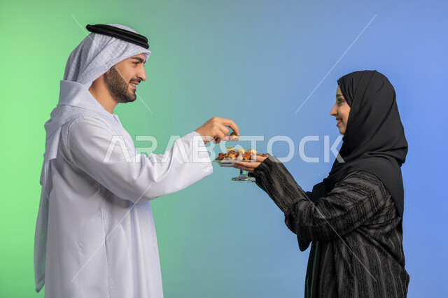 وجبة ذات قيمة غذائية عالية، بورتريه من الجانب لامراة عربية خليجية اماراتية ترتدي العباءة السوادء تقوم بتقديم التمر الصحي لزوجها، منتج زراعي محلي وطني ضيافة رمضانية لذيذة، افطار الصائم في رمضان، مفهوم احترام الزوج وتقديره، الاحتفال بقدوم شهر الخير