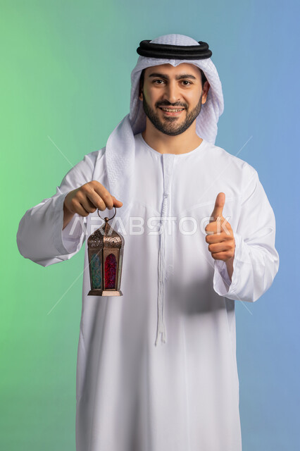 تعابير باصبع الابهام تدل على الاعجاب والقبول، المناسبات الدينية والأعياد الإسلامية, استقبال شهر الخير والبركة, الاستعداد لقدوم شهر رمضان, بورتريه مقرب لرجل عربي خليجي اماراتي يرتدي الغترة والكندورة التقليدية يحمل الفانوس وينظر الى الكاميرا بتعابير الفرح, تحف وزينة الاحتفالات في السعودية, خلفية ملونة