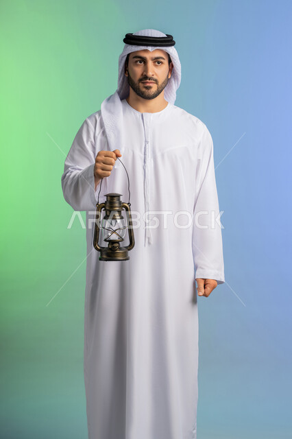 المناسبات الدينية والأعياد الإسلامية, استقبال شهر الخير والبركة, الاستعداد لقدوم شهر رمضان, بورتريه لرجل عربي خليجي اماراتي يرتدي الغترة والكندورة التقليدية يحمل الفانوس وينظر الى الكاميرا بتعابير الفرح, تحف وزينة الاحتفالات في السعودية, خلفية ملونة