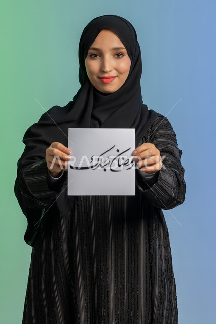 الاستعداد لاستقبال الشهر الفضيل, بهجة وفرحة المسلمين بقدوم شهر الخير،  بورتريه لسيدة عربية خليجية اماراتية مبتسمة ترتدي الحجاب والعباءة السوداء تقوم بعرض مخطوطة رمضان مبارك مزخرفة بإيماءات السرور والسعادة,  خلفية ملونة
