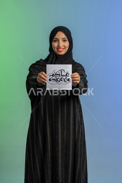 الاستعداد لاستقبال شهر رمضان المبارك, بهجة وفرحة المسلمين بقدوم شهر الخير،  بورتريه لسيدة عربية خليجية اماراتية مبتسمة ترتدي الحجاب والعباءة السوداء تقوم بعرض مخطوطة عساكم من عواده مزخرفة بإيماءات السرور والسعادة,  خلفية ملونة