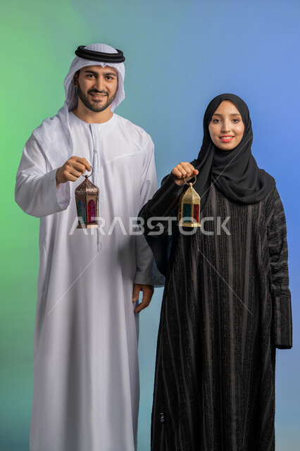 الإستعداد لرمضان المبارك, المناسبات الدينية والأعياد الإسلامية, بورتريه لرجل عربي خليجي اماراتي يرتدي الكندورة ويضع الغترة يقف مع زوجته ويحملان بايديهم فانوس رمضاني, سيدة عربية خليجية اماراتية ترتدي العباءة السوداء والحجاب تحتفل بقدوم الشهر الفضيل,  خلفية ملونة