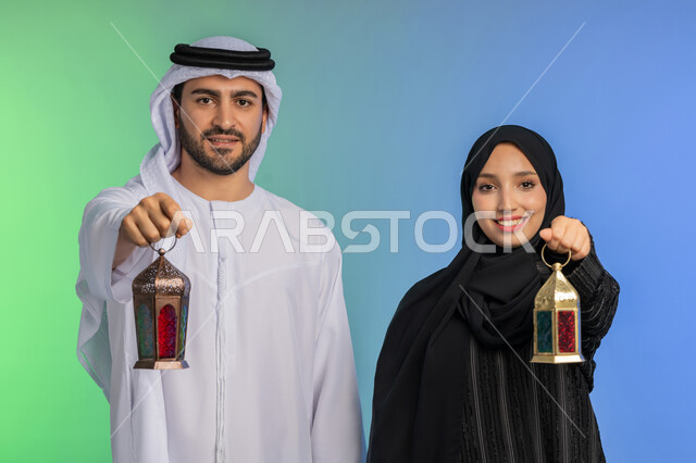 المناسبات الدينية والأعياد الإسلامية, بورتريه لرجل عربي خليجي اماراتي يرتدي الكندورة ويضع الغترة يقف مع زوجته ويحملان بايديهم فانوس رمضاني, سيدة عربية خليجية اماراتية ترتدي العباءة السوداء والحجاب تحتفل بقدوم الشهر الفضيل, الإستعداد لرمضان المبارك, خلفية ملونة