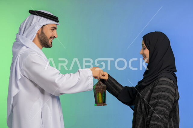 الاستعداد لقدوم رمضان, استقبال شهر الخير والبركة, المناسبة الدينية والعيد الإسلامي, بورتريه لرجل عربي خليجي اماراتي يرتدي الكندورة و الغترة التقليدية يقدم الفانوس لزوجته, تحف وزينة الاحتفالات في الامارات, خلفية ملونة