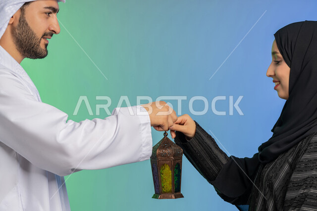 المناسبة الدينية والعيد الإسلامي, الاستعداد لقدوم رمضان, استقبال شهر الخير والبركة, بورتريه لرجل عربي خليجي اماراتي يرتدي الكندورة و الغترة التقليدية يقدم الفانوس لزوجته, تحف وزينة الاحتفالات في الامارات, خلفية ملونة