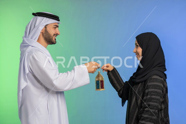الاستعداد لقدوم رمضان, استقبال شهر الخير والبركة, المناسبة الدينية والعيد الإسلامي, بورتريه لرجل عربي خليجي اماراتي يرتدي الكندورة و الغترة التقليدية يقدم الفانوس لزوجته, تحف وزينة الاحتفالات في الامارات, خلفية ملونة