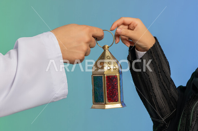 استقبال شهر الخير والبركة, المناسبة الدينية والعيد الإسلامي, الاستعداد لقدوم رمضان,  بورتريه مقرب ليد رجل عربي خليجي اماراتي يرتدي الكندورة و الغترة التقليدية يقدم الفانوس لزوجته, تحف وزينة الاحتفالات في الامارات, خلفية ملونة
