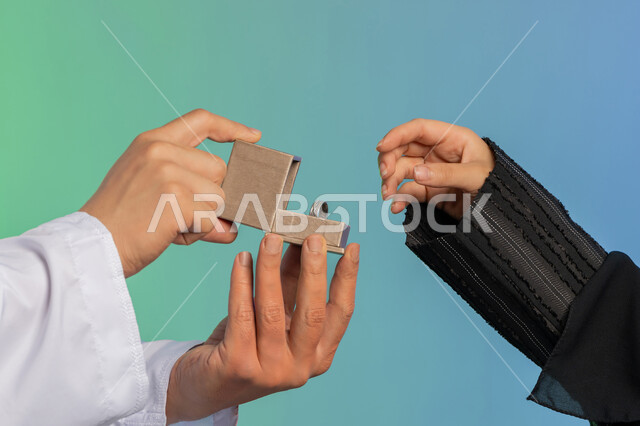 شراء مجوهرات ومحبس العروس، العادات والتقاليد للتقدم وطب الزواج، مفهوم الاستقرار وتكوين عائلة سعيدة، بورتريه مقرب ليد عريس عربي خليجي اماراتي يرتدي الكندورة يقوم بتقديم خاتم لزوجته، مراسم الأعراس في الامارات، خلفية ملونة