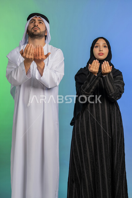 الاجتهاد في الطاعات والأدعية والأذكار، التمني والطلب من الله، ايماءات تدل على الخشوع والتضرع، العبادة والتقرب الى الله، بورتريه لزوجان  عربيان خليجيان اماراتيان يقومان برفع ايديهم بايماءات الدعاء، خلفية ملونة