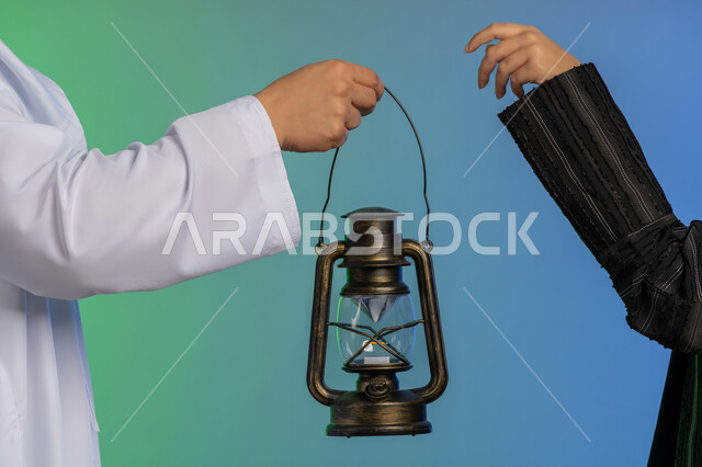 استقبال شهر الخير والبركة, المناسبة الدينية والعيد الإسلامي, الاستعداد لقدوم رمضان, بورتريه مقرب ليد رجل عربي خليجي اماراتي يرتدي الكندورة و الغترة التقليدية يقدم الفانوس لزوجته, تحف وزينة الاحتفالات في الامارات, خلفية ملونة