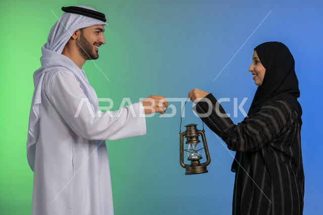 الاستعداد لقدوم رمضان, استقبال شهر الخير والبركة, المناسبة الدينية والعيد الإسلامي, بورتريه لرجل عربي خليجي اماراتي يرتدي الكندورة و الغترة التقليدية يقدم الفانوس لزوجته, تحف وزينة الاحتفالات في الامارات, خلفية ملونة