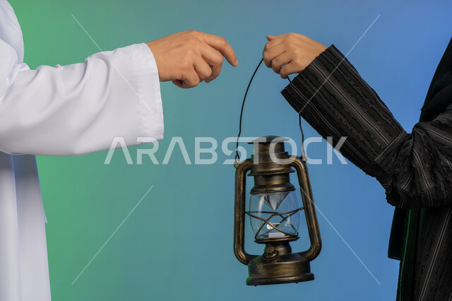 استقبال شهر الخير والبركة, المناسبة الدينية والعيد الإسلامي, الاستعداد لقدوم رمضان, بورتريه مقرب ليد رجل عربي خليجي اماراتي يرتدي الكندورة و الغترة التقليدية يقدم الفانوس لزوجته, تحف وزينة الاحتفالات في الامارات, خلفية ملونة