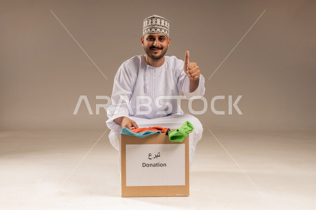 علامة الجودة والامتياز، جمعية خيرية ومبادرة انسانية في سلطنة عمان، تأمين الملابس للمحتاجين والفقراء، بورتريه لرجل عربي خليجي عماني يرتدي الدشداشة والكمة يرفع إصبع الإبهام ينظر إلى الكاميرا بإيماءات القبول والإعجاب، مفهوم المساعدة والتبرع، خلفية بيج
