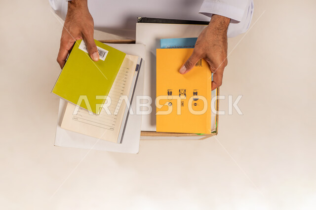 توفير المؤلفات التعليمية والكتب المفيدة للمحتاجين، بورتريه مقرب لرجل عربي خليجي عماني يرتدي الدشداشة يقوم باختيار كتاب من صندوق التبرعات، جمعية خيرية ومبادرة انسانية في سلطنة عمان، مفهوم المساعدة والتبرع، خلفية بيج