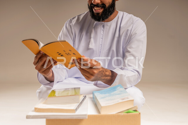 مفهوم المساعدة والتبرع، توفير المؤلفات التعليمية والكتب المفيدة للمحتاجين، بورتريه مقرب لرجل عربي خليجي عماني مبتسم يرتدي الدشداشة يقوم بتصفح واختيار كتاب من صندوق التبرعات، جمعية خيرية ومبادرة انسانية في سلطنة عمان، خلفية بيج