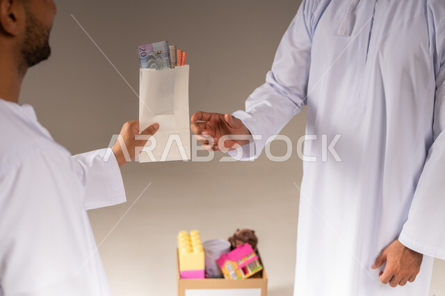 Charity and humanitarian initiative in the Sultanate of Oman, the concept of assistance and donation, close-up portrait of an Arab Gulf Omani man wearing a dishdasha holding an envelope of paper money that he is giving to another person, getting closer to God through giving and charity, giving zakat money to the needy, beige background