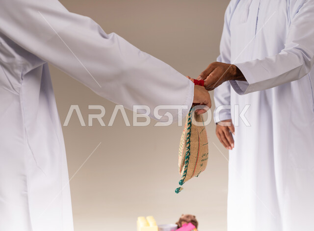 إخراج زكاة الحبوب للفقراء، مفهوم المساعدة والتبرع، بورتريه مقرب لرجل عربي خليجي عماني يرتدي الدشداشة يقوم بتقديم كيس من الأرز لشخص آخر، جمعية خيرية ومبادرة إنسانية في سلطنة عمان، التقرب إلى الله بالعطاء والصدقة للمحتاجين، خلفية بيج