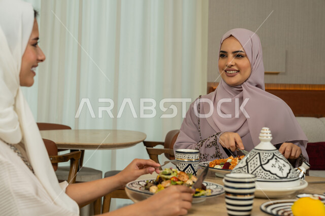 الاستمتاع بقضاء الوقت برفقة الأصدقاء، جلسة وناسة في عطلة نهاية الاسبوع, ايماءات السعادة والسرور، اجتماع الرفاق في مطعم فاخر بالامارات، صديقتين عربيتين خليجيتين اماراتينين تجلسان على طاولة طعام مليئة بالأطعمة والمأكولات الشهية، سيدتان سعوديتان تتناولان العشاء