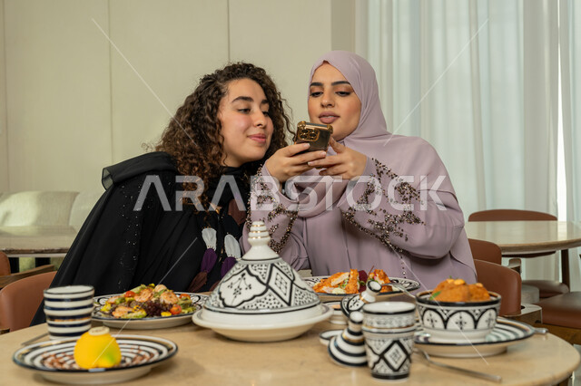 التقاط الصور التذكارية عبر الهاتف المحمول، اجتماع الرفاق على طاولة طعام في مطعم فاخر بالامارات، قضاء وقت ممتع برفقة الأصدقاء في عطلة نهاية الاسبوع، صديقتين عربيتين خليجيتين اماراتيتين تقومان بتناول العشاء معا في الخارج، سيدتان سعوديتان تجلسان على المائدة