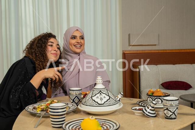 جلسة وناسة في عطلة نهاية الاسبوع, ايماءات السعادة والسرور، اجتماع الرفاق على طاولة طعام في مطعم فاخر بالامارات، قضاء وقت ممتع برفقة الأصدقاء، صديقتين عربيتين خليجيتين اماراتيتين تقومان بتناول العشاء معا في الخارج، سيدتان سعوديتان تجلسان على المائدة